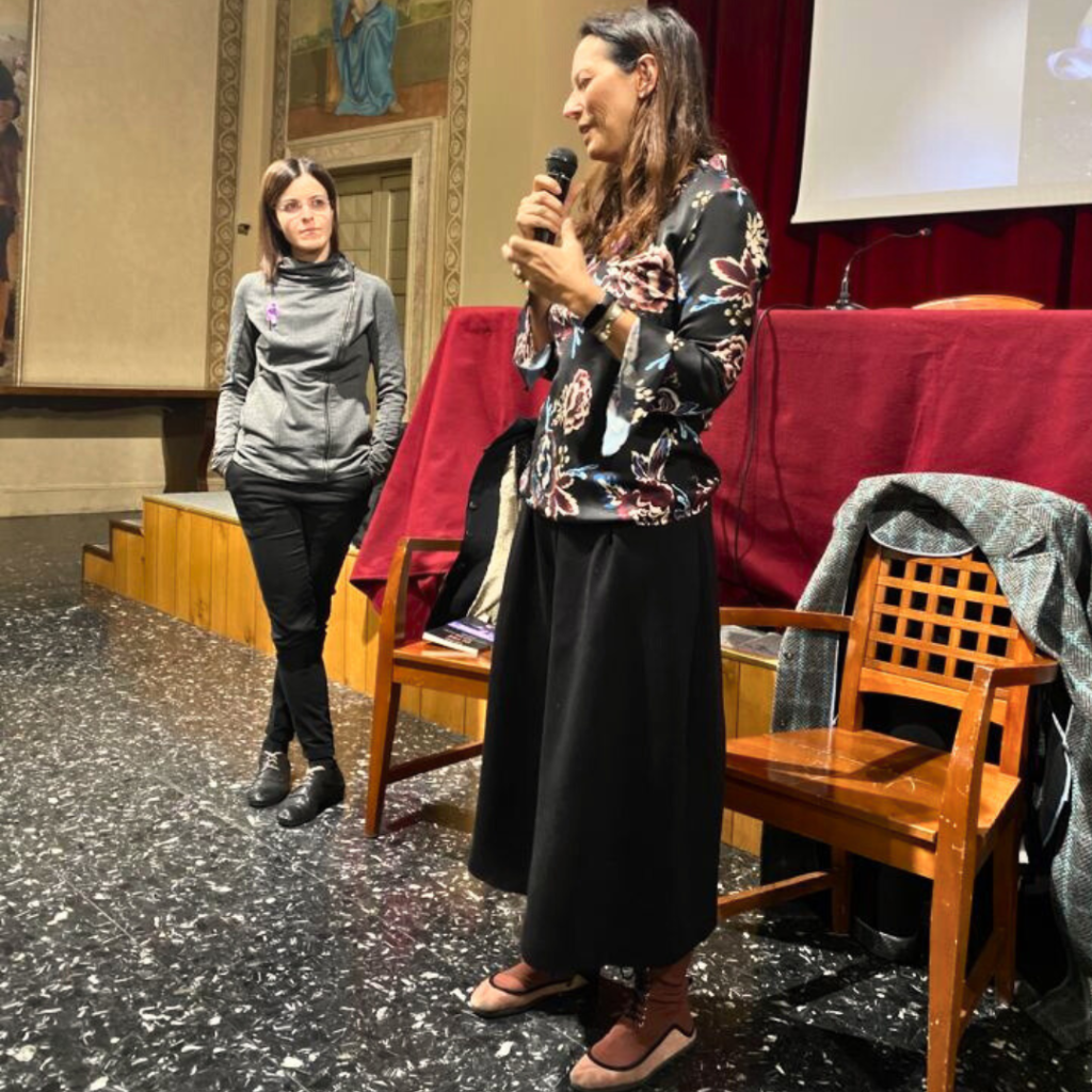 Nella foto due donne, una più in primo piano dell'altra. É la regista Carola Minincleri Colussi. In secondo piano in piedi a gambe incrociate e mani in tasca la scrittrice Sandra Zodiaco, autrice del libro "Oltre. Confessioni sul (mio) disturbo alimentare".